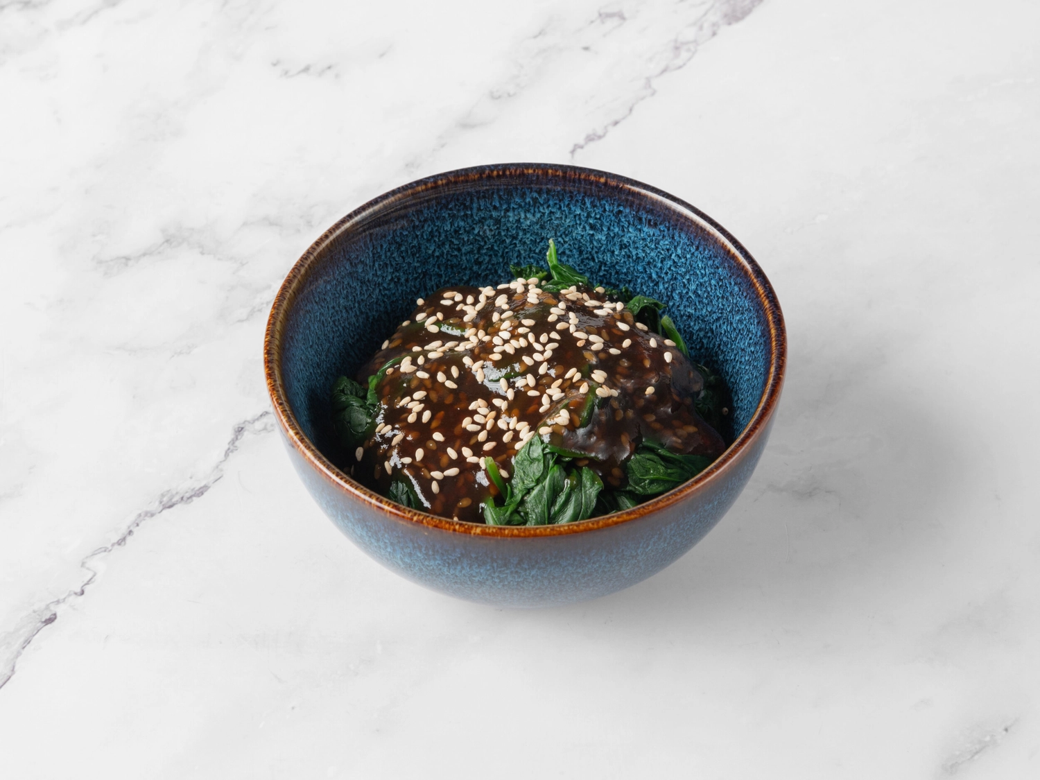 Restaurant Strassfeld - Sushi & moderne Küche - Dieses Gericht scheint eine Beilage von Spinat oder ähnlichem Gemüse zu sein, die mit einer herzhaft-süßen Glasur überzogen ist, wahrscheinlich auf Teriyaki- oder Miso-Basis, garniert mit Sesamkörnern.